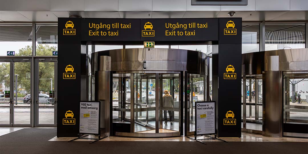 iStock-1786654222_SM_taxi_utgång_1080x540px Svenska: Ingång till taxizonen med snurrdörr och skyltar med texten ”Utgång till taxi” och symboler för taxi. English: Entrance to the taxi zone with a revolving door and signs reading “Exit to taxi” with taxi symbols.