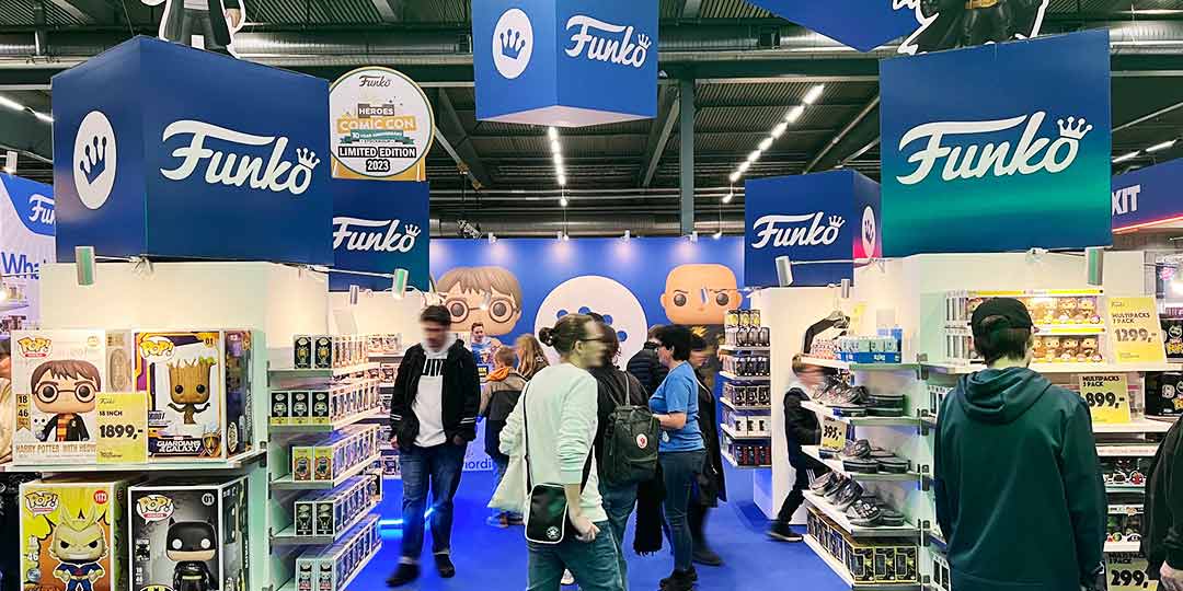 Bli utställare 2 monteryta från comicon på Stockholsmässan med vita hyllor, blåa hängande boxar med logor på