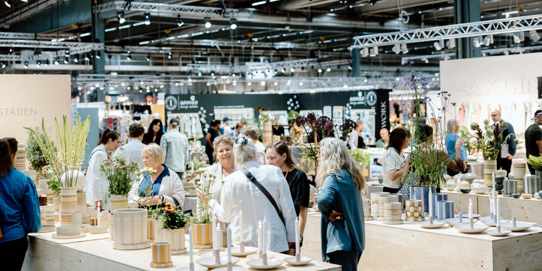 Mässbesökare tittar på inredningsprodukter och växter i en välbesökt utställningshall på Stockholmsmässan.